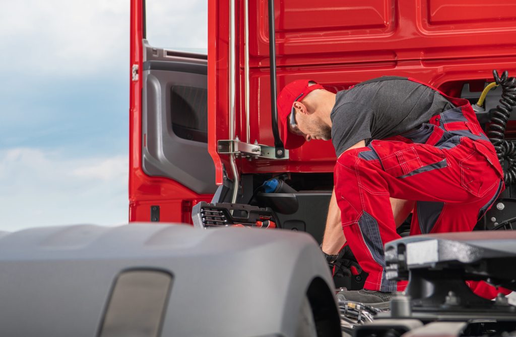 Professional Caucasian Truck Mechanic in His 40s Wearing Red Uniform Performing Modern Semi Truck Repair. Transportation Industry.